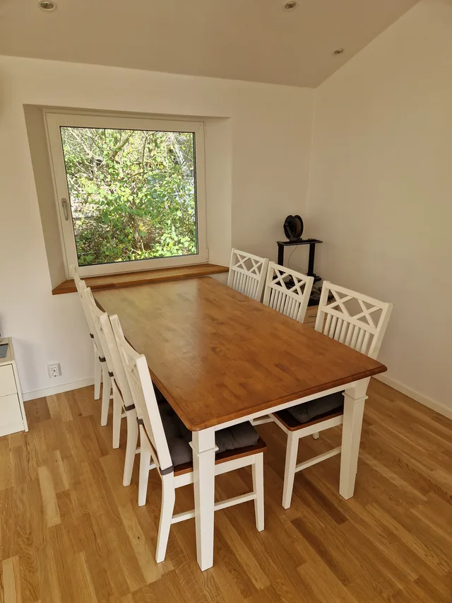Matplats med träbord, vita stolar och fönster mot trädgården