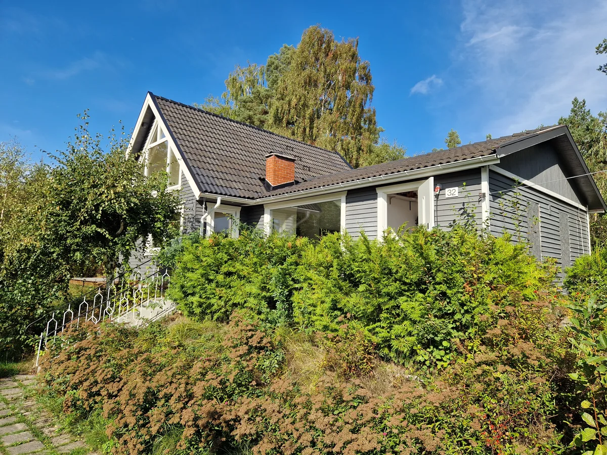 Det grå huset med vita detaljer, inramat av häckar och träd
